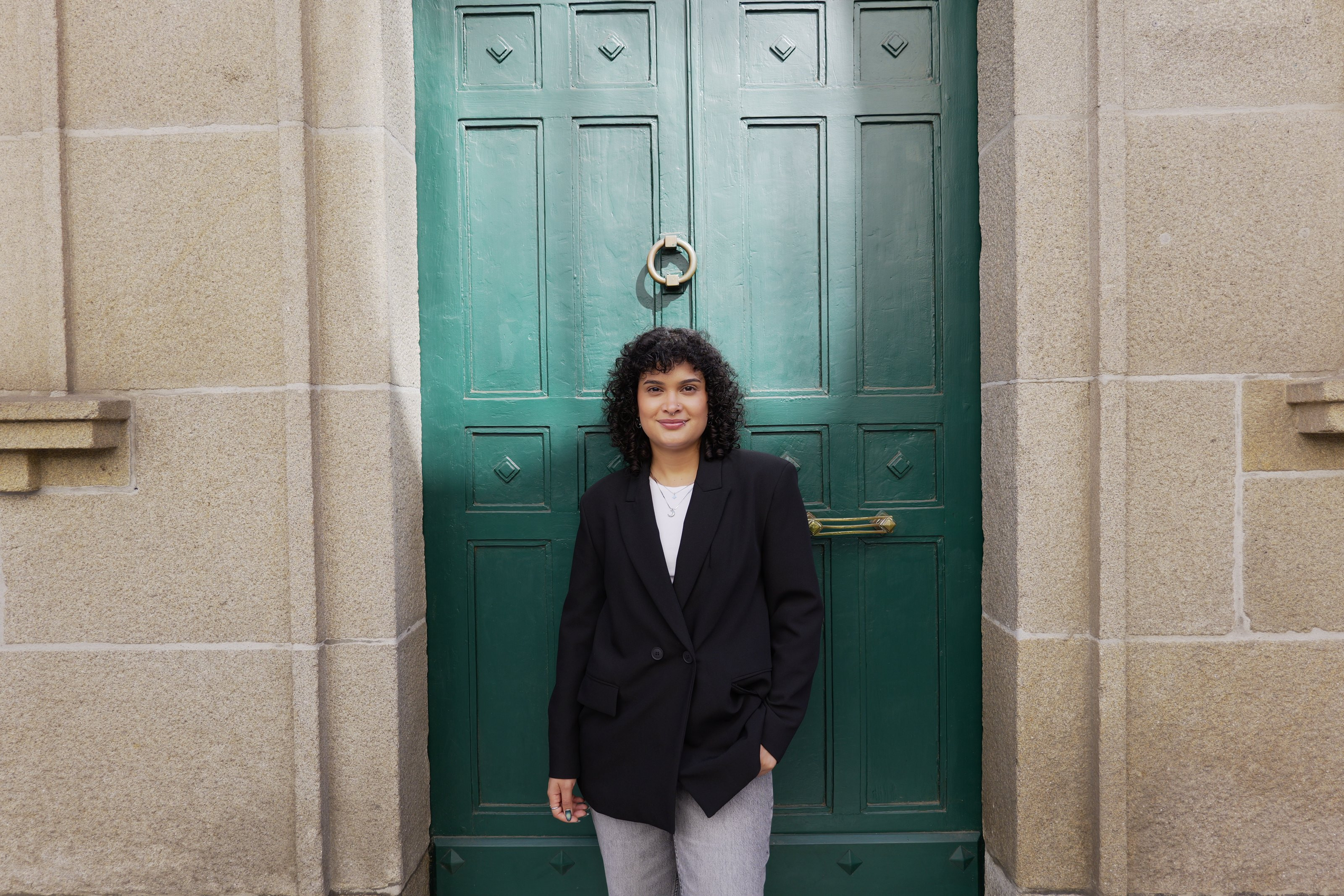 Verónica con blazer negro frente a una puerta verde entre muros de granito